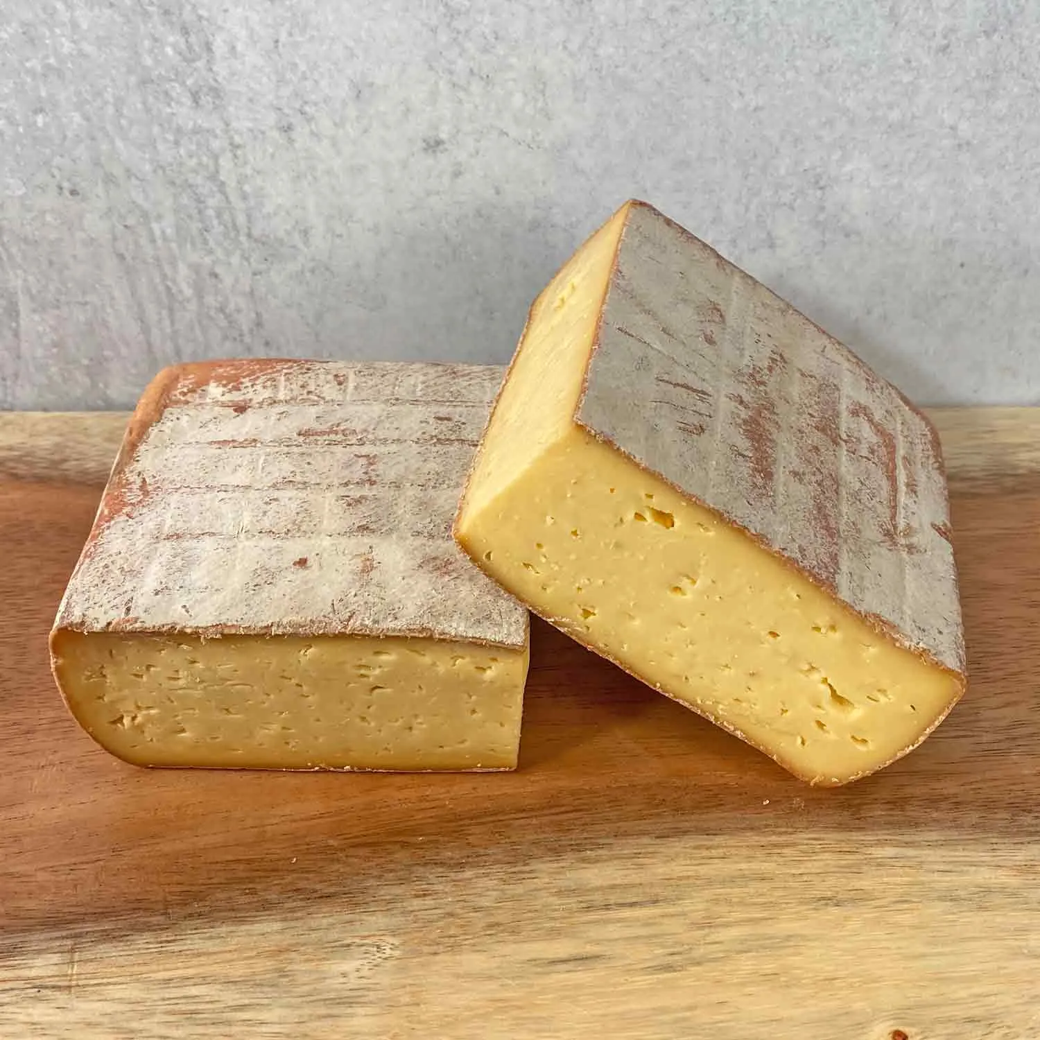 Pieces of Grayson cheese, showcasing a reddish-orange rind and golden interior, arranged on a wooden surface.