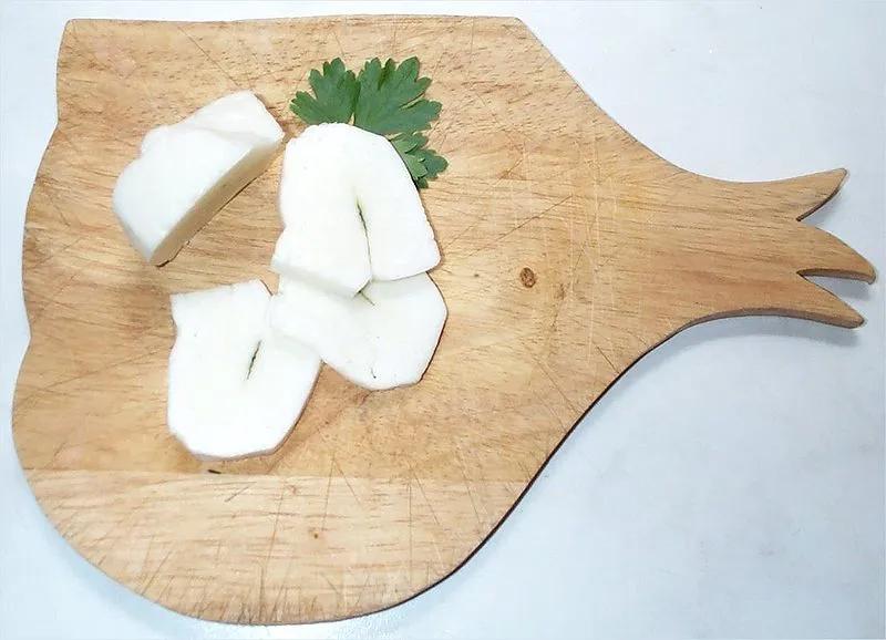 Fresh sliced Halloumi cheese with a whole leaves of mint in the middle of a wooden board.