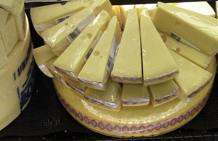 Slices of Jarlsberg cheese arranged atop a whole wheel, showcasing its pale yellow color