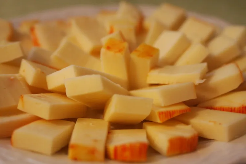 Rectangular slices of Muenster cheese, with a pale yellow interior and orange rind, arranged neatly on a wooden plate