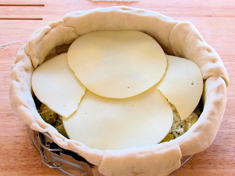 Thin, round slices of Provolone cheese arranged on top of a stuffed pizza in a springform pan, ready to bake