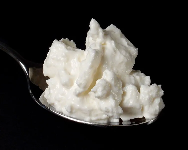 Quark on a spoon, showcasing its soft and creamy texture against a black background