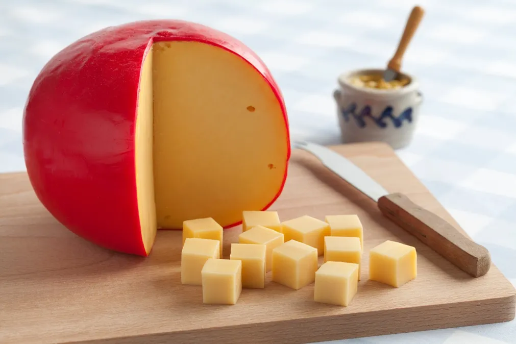 Edam cheese with a red wax coating, cut into cubes and arranged on a cutting board