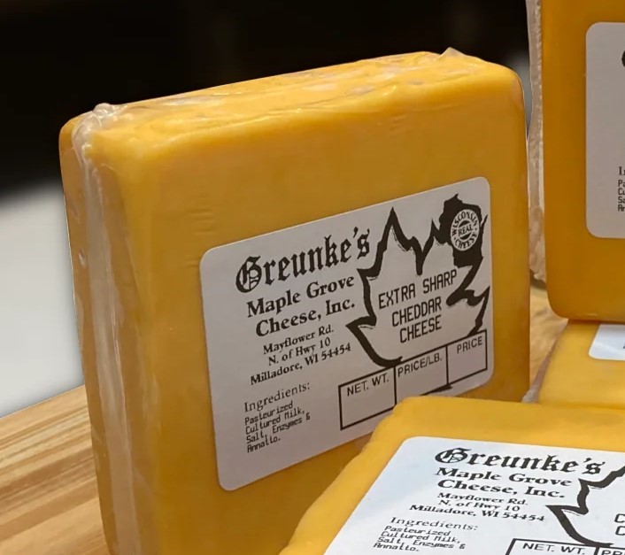 Block of Extra Sharp Cheddar, wrapped in plastic with label rests on a wooden table.