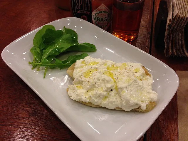 Ricotta cheese spread over a slice of pizza, with fresh spinach leaves, arranged on a white rectangular plate